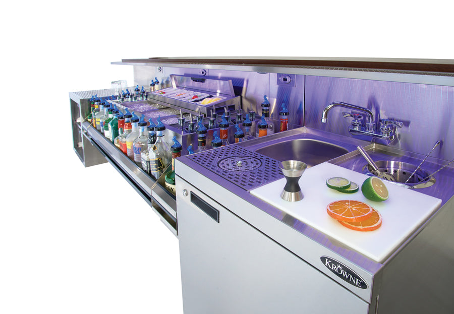 Beverage preparation station with bottles, a cutting board with fruits, and a sink.